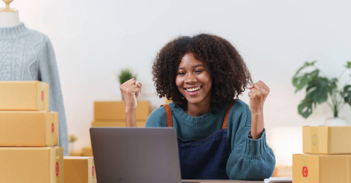 Mulher em frente ao notebook comemorando vendas online que fez na sua loja